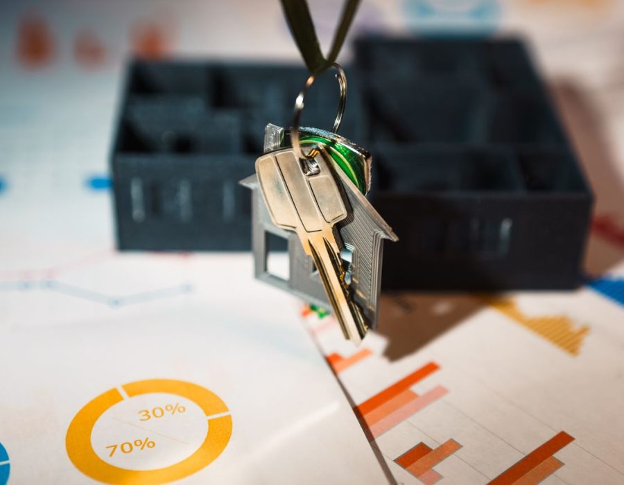 Real estate keys on house keychain with financial graphs, symbolizing property investment.